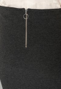 Schwarzer Strickrock mit horizontaler Rippstruktur und einem silbernen Reißverschlussverschluss auf der Rückseite. Glattes Material mit strukturiertem Schnitt.