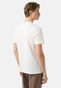 Biały bawełniany t-shirt z krótkimi rękawami, okrągłym dekoltem i luźnym krojem. Tył ma gładką teksturę i staranne szwy.