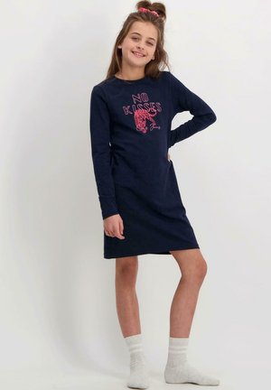Marineblauwe jurk met lange mouwen met de tekst "NO KISSES" en een afbeelding. Gemaakt van zacht katoen; knielengte en een losse pasvorm. Draagt witte sokken.