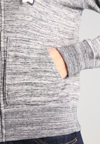 Hoodie grigio melange con tasca a marsupio frontale, polsini a costine e un tessuto morbido e testurizzato.