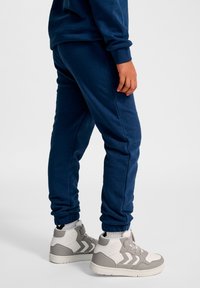 Granatowe spodnie dresowe z elastycznymi ściągaczami i bocznymi szwami, zestawione z białymi i szarymi butami typu high-top z teksturowanymi detalami.
