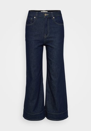 Donkerblauwe denim jeans met wijde pijpen, voorzien van een knoop- en ritsluiting aan de voorkant en een vijf-pocket ontwerp, gepresenteerd op een effen lichte achtergrond.