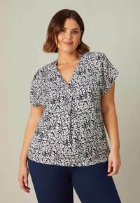 Kortärmad blus i svart och vitt blommönster, med v-ringning och plisserad front, tillverkad av lättviktsmaterial.