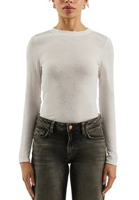 Langärmliges weißes, geripptes Oberteil mit verstreuten Strasssteinen, Rundhalsausschnitt, kombiniert mit dunkelgrauer Denim-Jeans. Weiche Textur, figurbetontes Design.