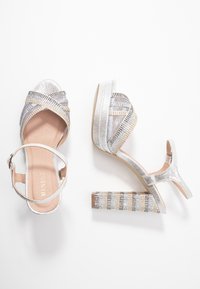 Stříbrné sandály na vysokém podpatku s křížovými pásky, texturovaným povrchem a pruhovaným blokovým podpatkem zdobeným kamínky.