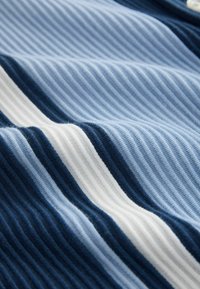 Gros plan sur un tissu côtelé avec des rayures horizontales en bleu clair, bleu foncé et blanc sur une surface textile texturée.