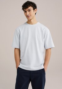 Svetlo modra kratka majica z dolgimi rokavi iz bombaža. Ima okroglo ovratnik in sproščen kroj, v kombinaciji s temno modrimi hlačami.