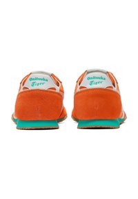 Sneakers in suede arancione con accenti bianchi, forma tondeggiante, suola verde e logo "Onitsuka Tiger" sul tallone. Design minimalista.