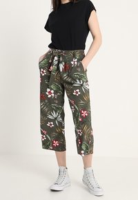 Cropped, floral-patterned trousers in dark green, featuring a drawstring waist and side pockets, paired with a black short-sleeve top and white sneakers.