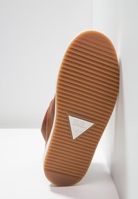 Suela de zapatilla marrón con estrías verticales, ribete blanco y un logotipo triangular "HUB". Material de goma con una superficie texturizada para mayor agarre.