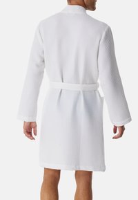 Accappatoio in cotone bianco a nido d'ape con maniche lunghe, vita con cintura e superficie testurizzata. Presenta un colletto a scialle e tasche laterali.
