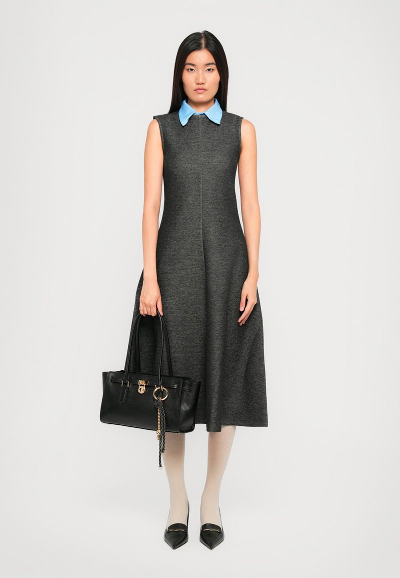 Woman wearing a sleeveless dark gray midi dress with a blue collar, holding a black handbag, paired with white tights and black pointed shoes.