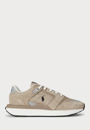 Beige og hvid sneaker med mesh- og ruskindsteksturer, hvide snørebånd, sort logo på siden og tyk hvid sål med sort mønster.