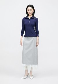 Tricou polo bleumarin cu mâneci lungi și guler cu nasturi, asortat cu o fustă lungă gri, cu tiv din dantelă albă și pantofi albaștri cu vârf ascuțit.