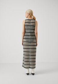 Robe maxi avec des motifs rayés noir et crème, sans manches, avec une fente dans le dos. Associée à des bottines blanches. Texture lisse.