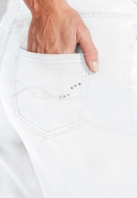 Witte denim jeans met een close-up van de achterzak, met een decoratief gestikt ontwerp en kleine zilveren studs.