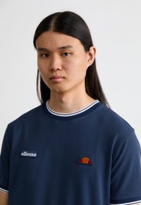 Marine crew-neck t-shirt lavet af bomuld, der har en hvid stribet ribkant, broderet logo og farvet motiv på brystet.