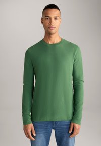 Groen langemouwen top in textuurstof, met een ronde hals en aansluitende mouwen, gecombineerd met blauwe denim jeans.