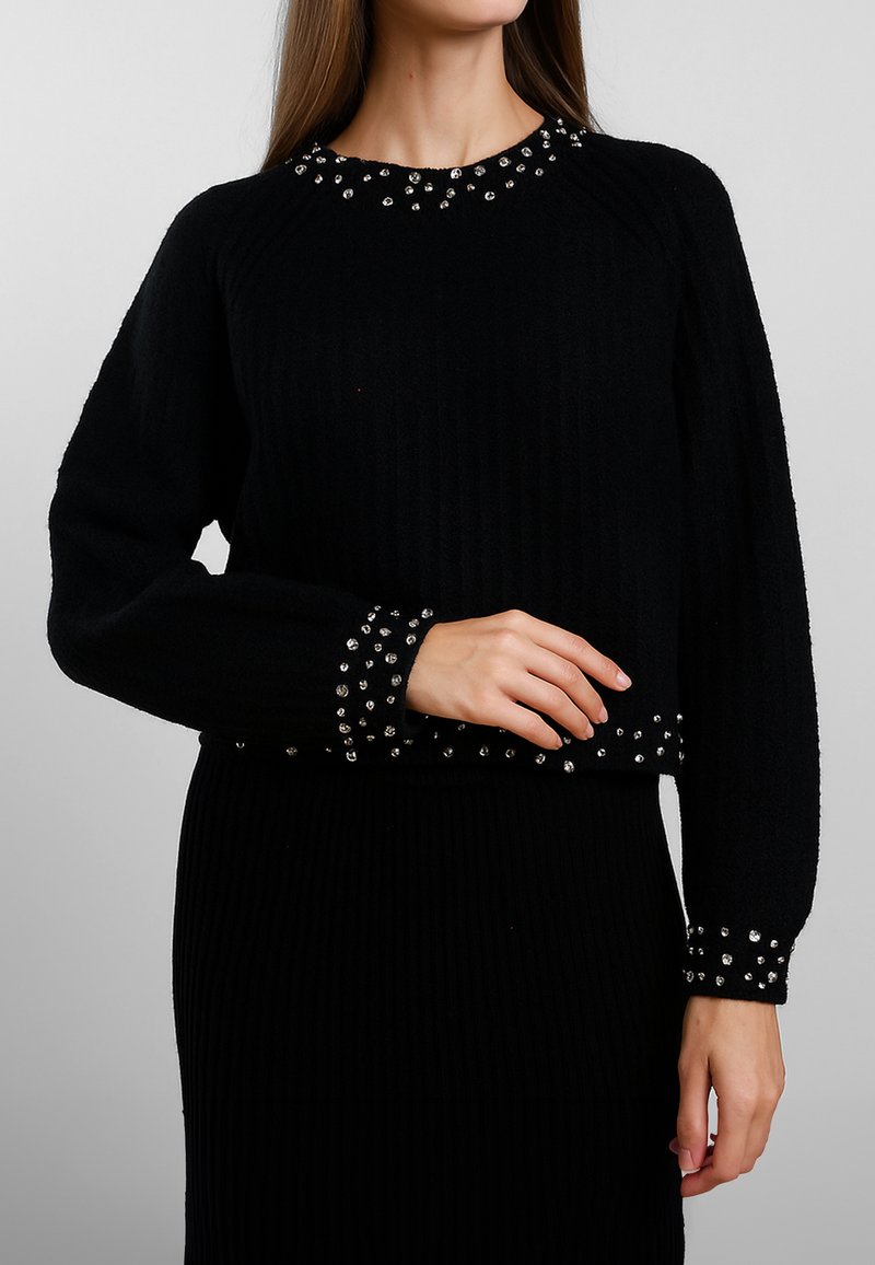 Maglione nero a coste con scollatura rotonda arricchita da borchie argentate e dettagli coordinati con borchie sui polsini, realizzato in morbido materiale lavorato a maglia.