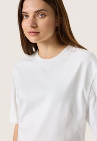 Witte katoenen t-shirt met een ronde halslijn en korte mouwen. Heeft een fijne textuur en lichte zijsamendetails.