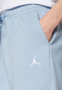 Světlé modré tepláky vyrobené z měkké látky, s elastickým pasem, bočními kapsami a bílým vyšitým logem Jumpman.