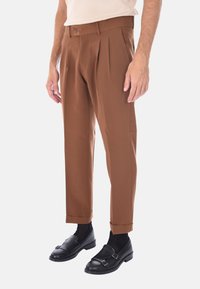 Pantaloni marroni plissettati con una vestibilità su misura, caratterizzati da una superficie liscia e orlo risvoltato, abbinati a mocassini neri e calzini scuri.