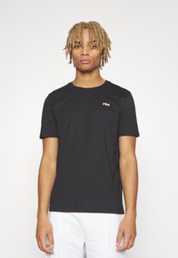 Camiseta de algodón negra de manga corta, con un pequeño logo de Fila en rojo y blanco en la zona izquierda del pecho. Diseño sencillo de cuello redondo.