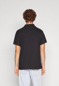 Polo negro con cuello clásico, mangas cortas y un corte relajado. Confeccionado con una tela suave, presenta sutiles detalles de costura.