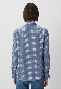 Blå mönstrad skjorta med geometrisk design, långärmad och med krage. Tyget har en slät textur och en något lös passform.