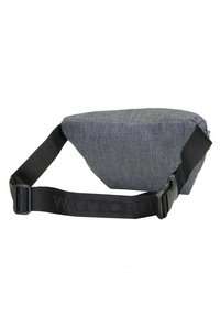 Šedá látková crossbody taška s ostrými tvary, texturovaný materiál a nastavitelné černé rameno s vyraženým logem. Viditelné zapínání na zip.