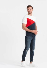 Camiseta de manga corta con bloques de color blanco, rojo y navy. Complementada con jeans de mezclilla oscura y zapatillas blancas. Textura de algodón suave.