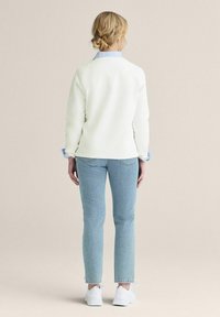 Vit sweatshirt med blå krage, matchad med ljusblå jeans. Sneakers fulländar looken; mjuk textur och avslappnad passform.