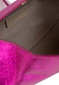 Pink glitter håndtaske indvendig med en glat beige foring, en rektangulær lomme og subtile syninger langs sømmen.