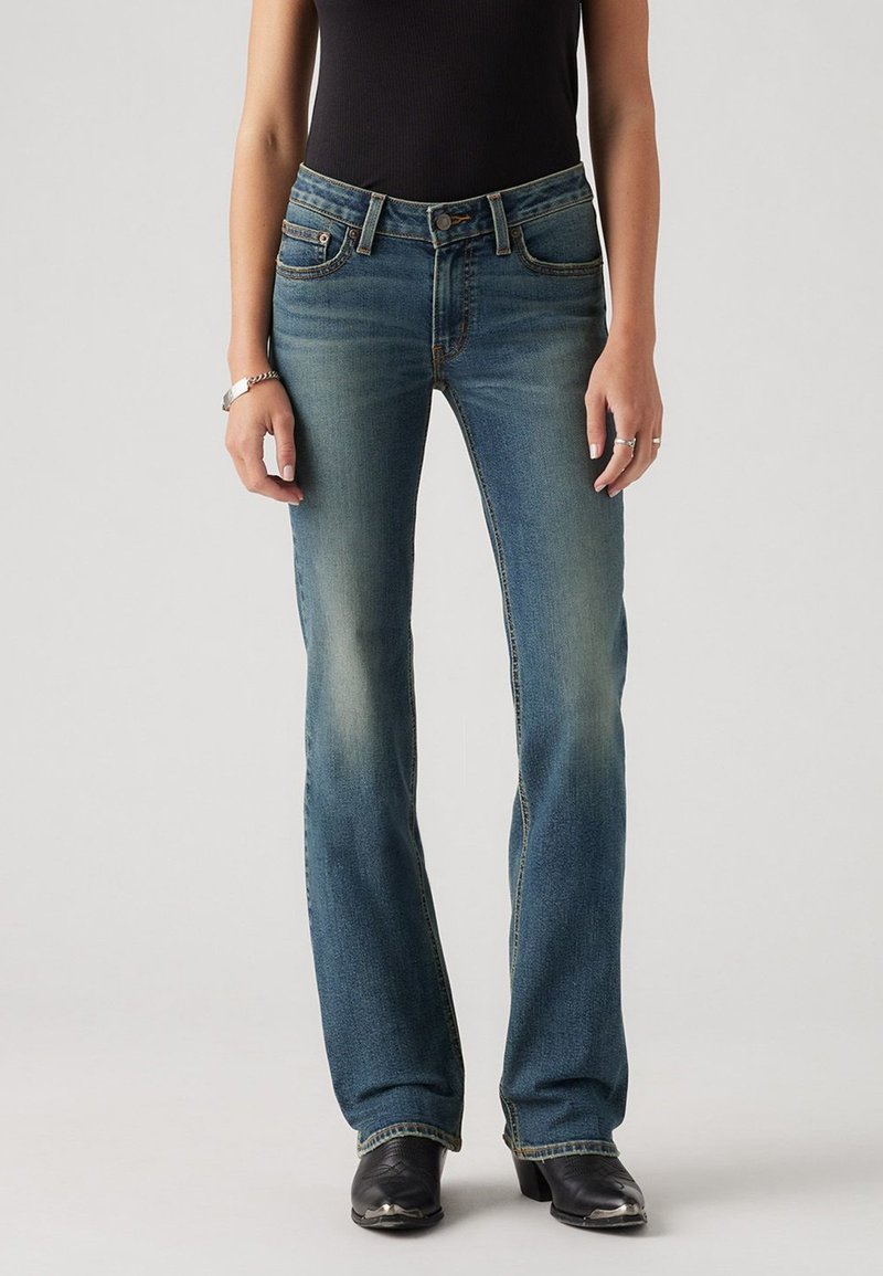 Blue denim jeans with a fitted waist and flared legs, featuring fading details, stitching accents, and a classic five-pocket design.