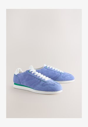 Semišové tenisky ve světle fialové barvě s bílými tkaničkami a zelenými detaily. Mají bílou gumovou podrážku s texturovaným gripem. Klasický design.