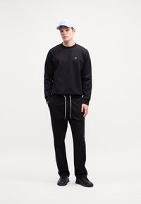 Sort sweatshirt med rund halsudskæring og logo, parret med sorte joggers med snoretræk. En lyseblå kasket og sorte sneakers fuldender outfittet.