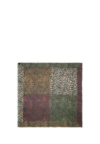 Textil de estampado de leopardo con diseño de patchwork en tonos tierra: marrón, verde, rojo y crema, con patrones de manchas variados y bordes deshilachados.