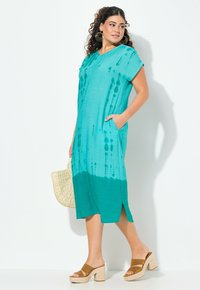 Türkises und grünes Batik-Midikleid mit kurzen Ärmeln, Seitentaschen und einer schlanken Silhouette. Verfügt über einen leicht strukturierten Stoff.