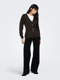 Brauner V-Ausschnitt Cardigan mit Knöpfen; lange Ärmel; kombiniert mit weißem Top und schwarzen Schlaghosen; glatte Textur und legeres Design.