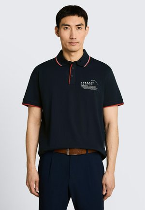 Mężczyzna noszący czarną koszulkę polo z czerwonym obszyciem i białym napisem „Forever Summer Tropical Paradise”, stojący na jednolitym tle.