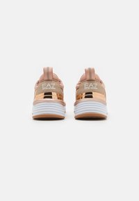 Athletic shoes with a pink and metallic gold upper, white and beige sole, pull tab at the back, and EA7 branding on the heel.