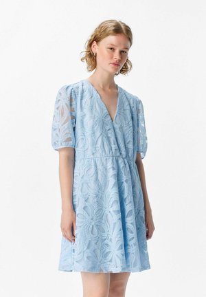 Lyseblå kjole lavet af guipure, med puffærmer, en dyb V-udskæring og blomster mønstre i hele stoffet. Udfoldet, over knæ-længde.
