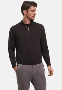 Pullover a maglia marrone scuro con colletto a mezza zip, polsini e orlo a costine, abbinato a pantaloni grigi chiari con tessuto testurizzato.