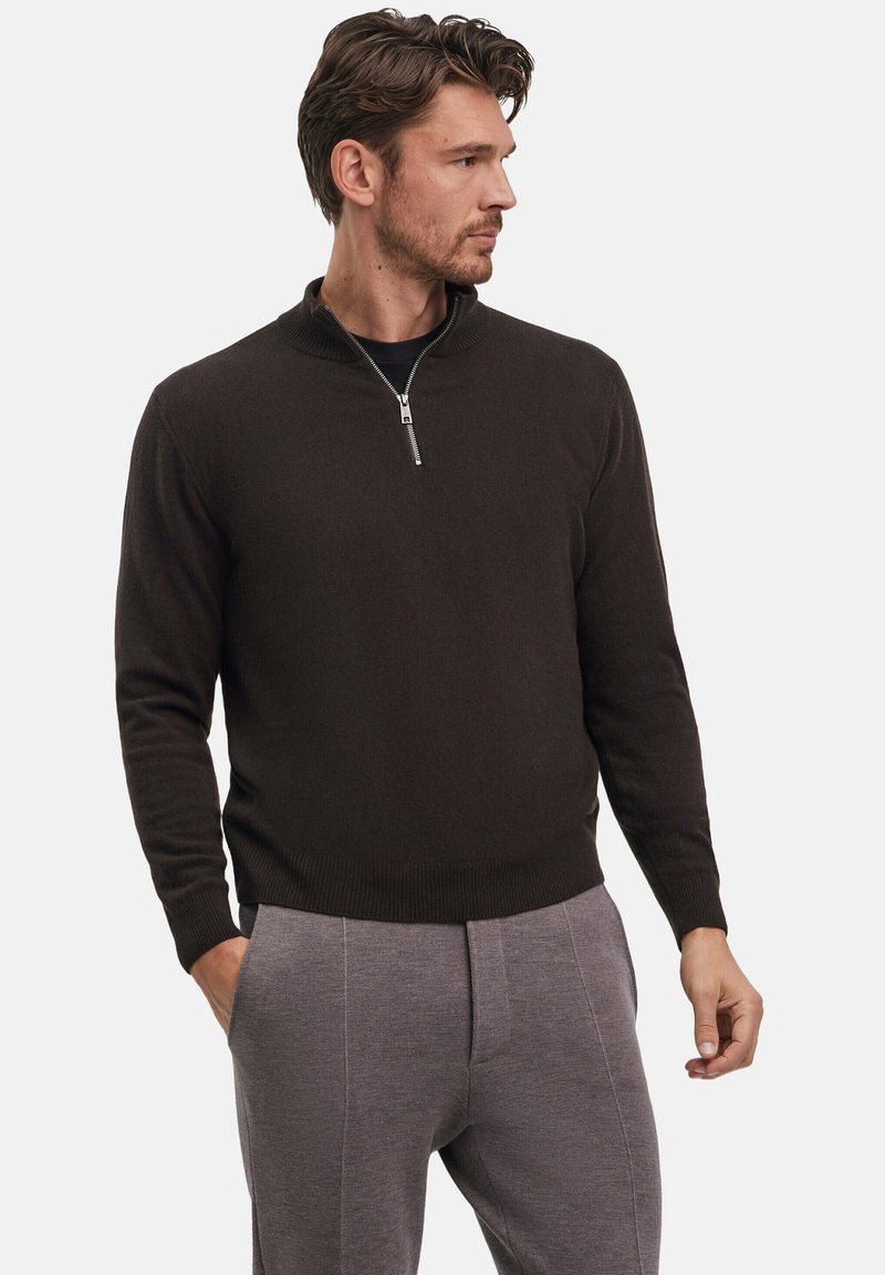 Pullover a maglia marrone scuro con colletto a mezza zip, polsini e orlo a costine, abbinato a pantaloni grigi chiari con tessuto testurizzato.