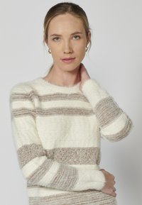 Kootud sviiter, millel on horisontaalsed triibud kreemi- ja pruunikasbeeži värvitoonis, pehme tekstuuriga viimistlus ja ümmargune kaelus. Pikad varrukad mansettidega.