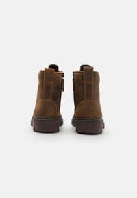 Stivali alla caviglia in suede marrone con finitura texturizzata, zip sul retro e linguetta per il tallone; suola in gomma robusta con un leggero tacco.