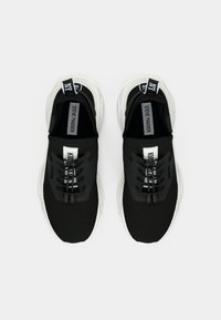 Black and white Steve Madden sneakers with textured upper, elastic no-tie laces, and branded pull tabs on white background.