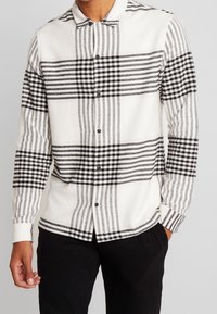 Een button-up shirt in een zwart-wit geruit patroon, gemaakt van een gestructureerde stof met lange mouwen en een kraag. Voorzien van zwarte knopen.