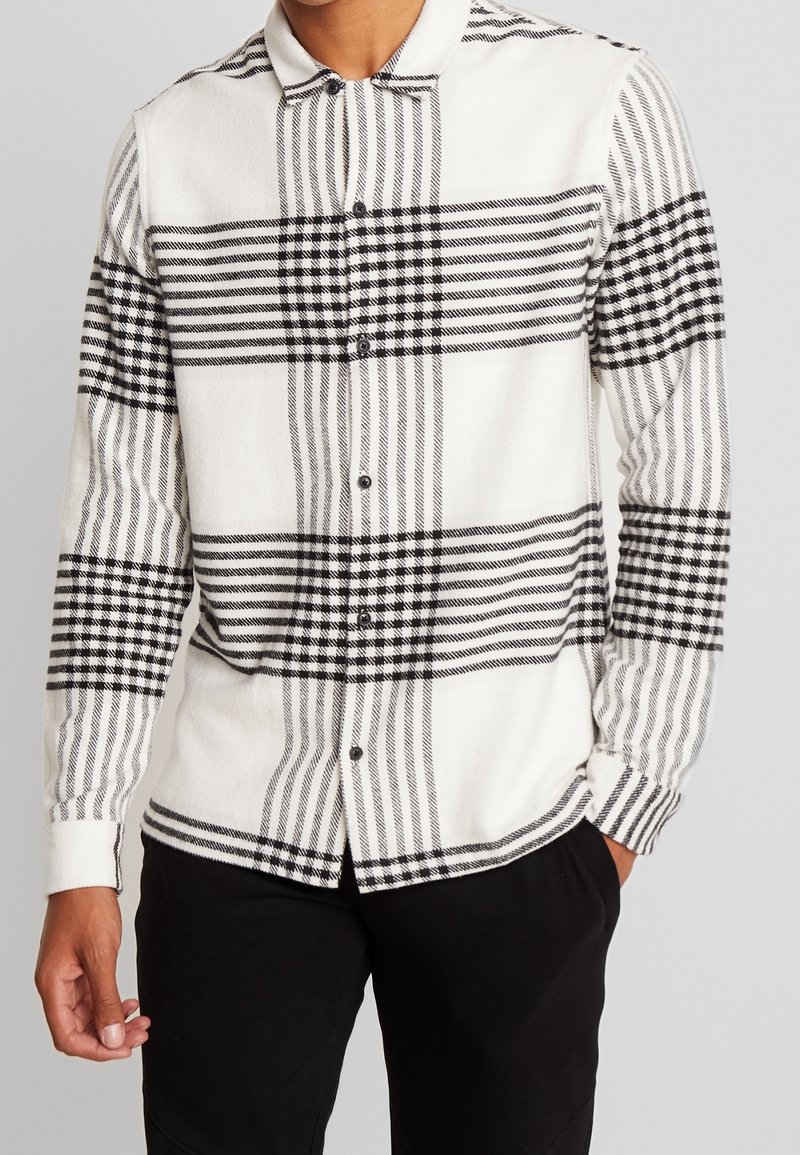 Een button-up shirt in een zwart-wit geruit patroon, gemaakt van een gestructureerde stof met lange mouwen en een kraag. Voorzien van zwarte knopen.