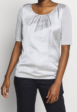 Haut gris clair à manches courtes avec un col rond et un détail de plissage froncé à l'avant. Tissu lisse, légèrement brillant et de forme ajustée.